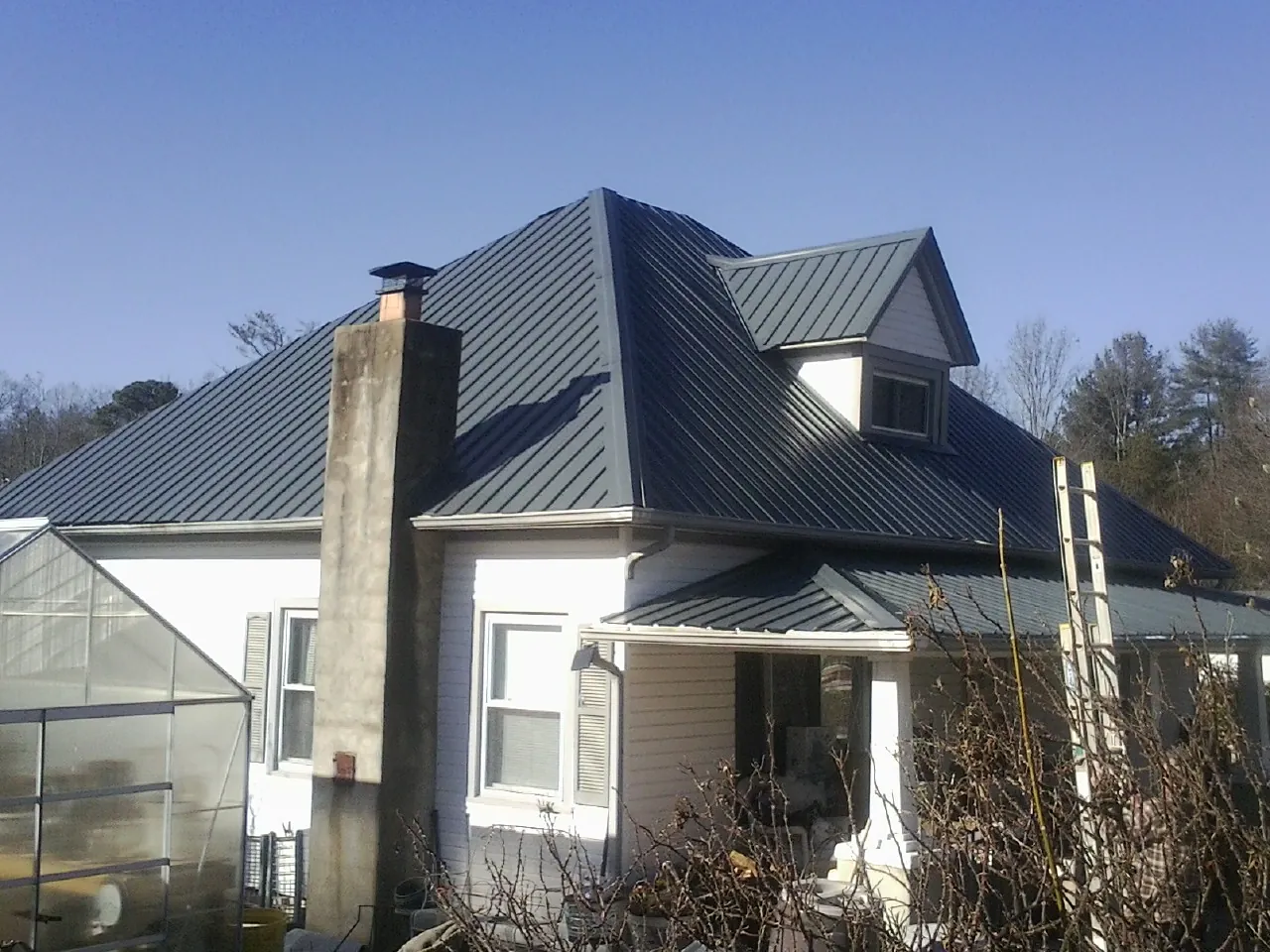 Dark blue standing seam metal roof on a white farmhouse with dormer — Slate & Tile Roof Repair by Roofing Brothers in Burgoon