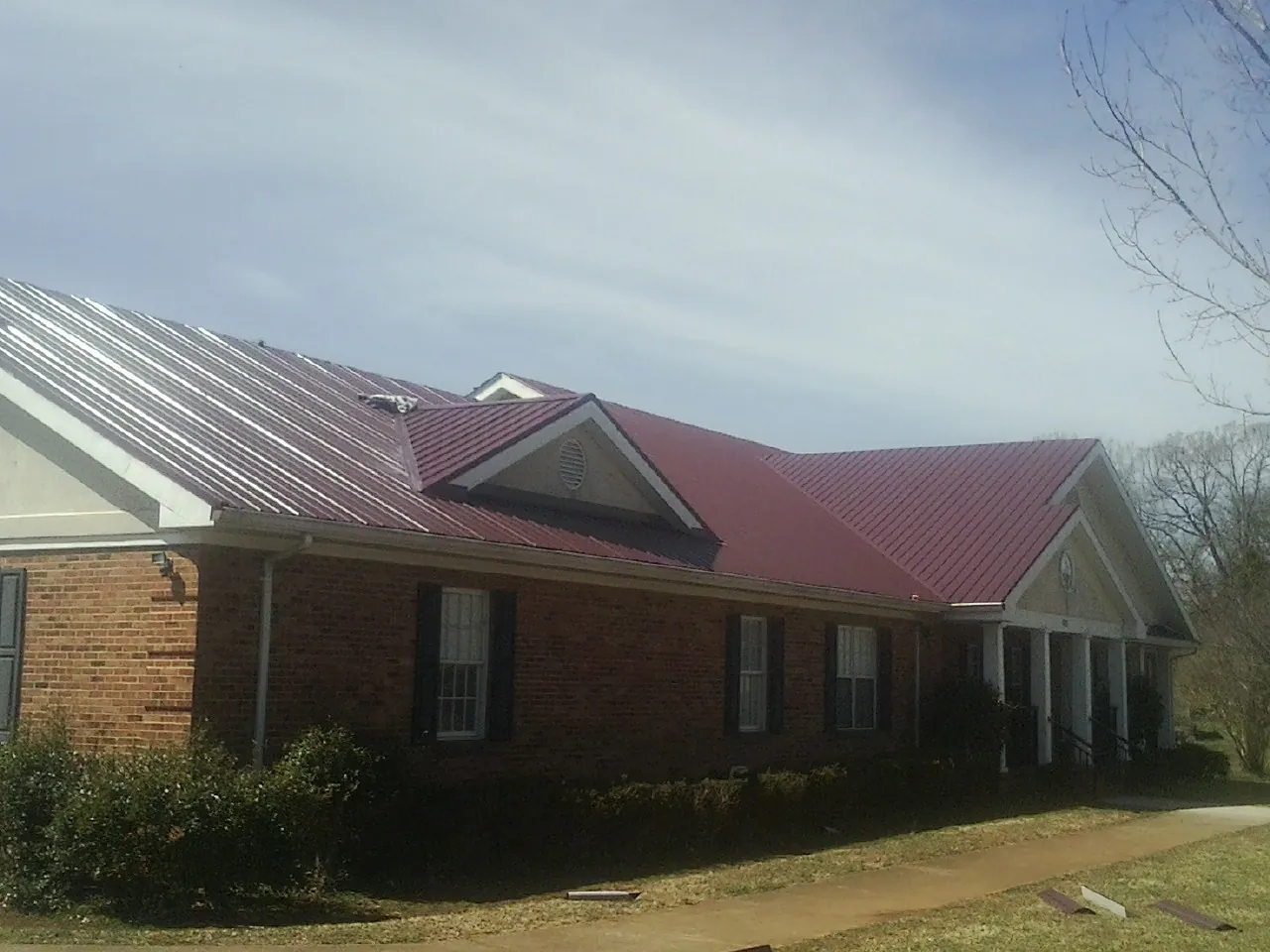 Red metal roof with gabled entries on a long brick building, from a Hail Damage Roof Repair job in Burgoon