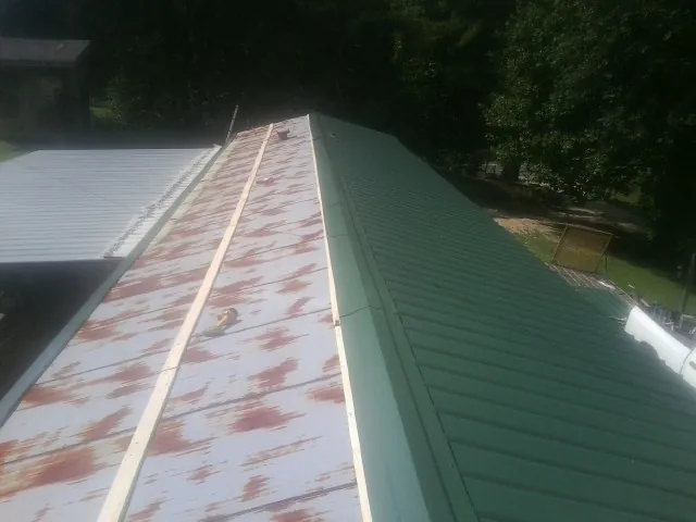 Old rusted panels beside newly installed green metal roofing — Wind Damage Roof Repair by Roofing Brothers in Burgoon