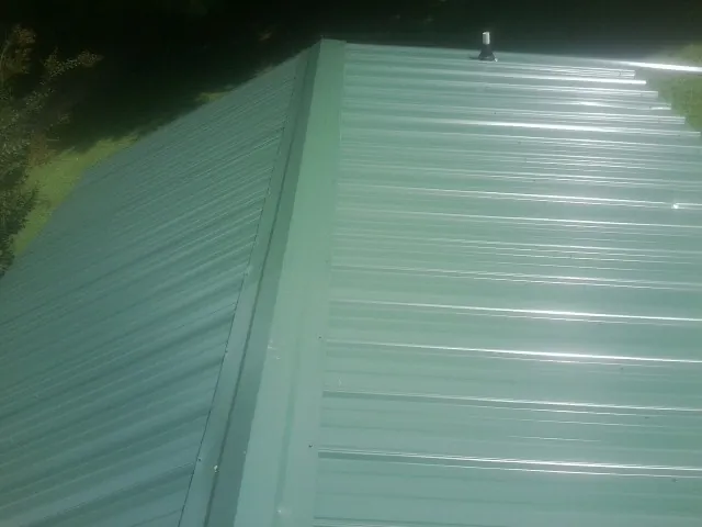 New green metal panels meeting at the ridge of a roof — Flat Roof Repair work by our crew in Burgoon