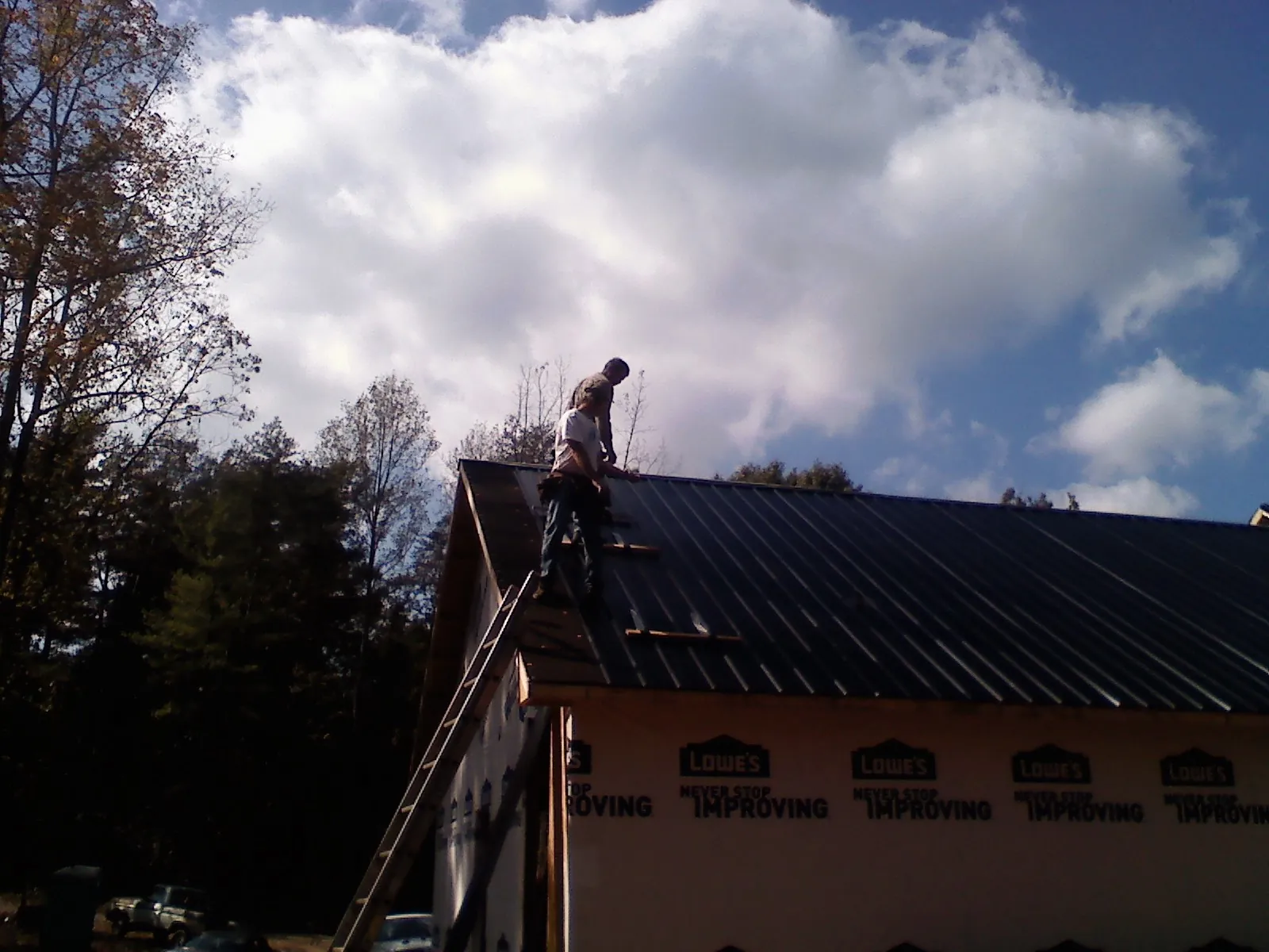 Roofer fastening dark metal panels high against a cloudy sky, from a Roof Inspection job in Burgoon