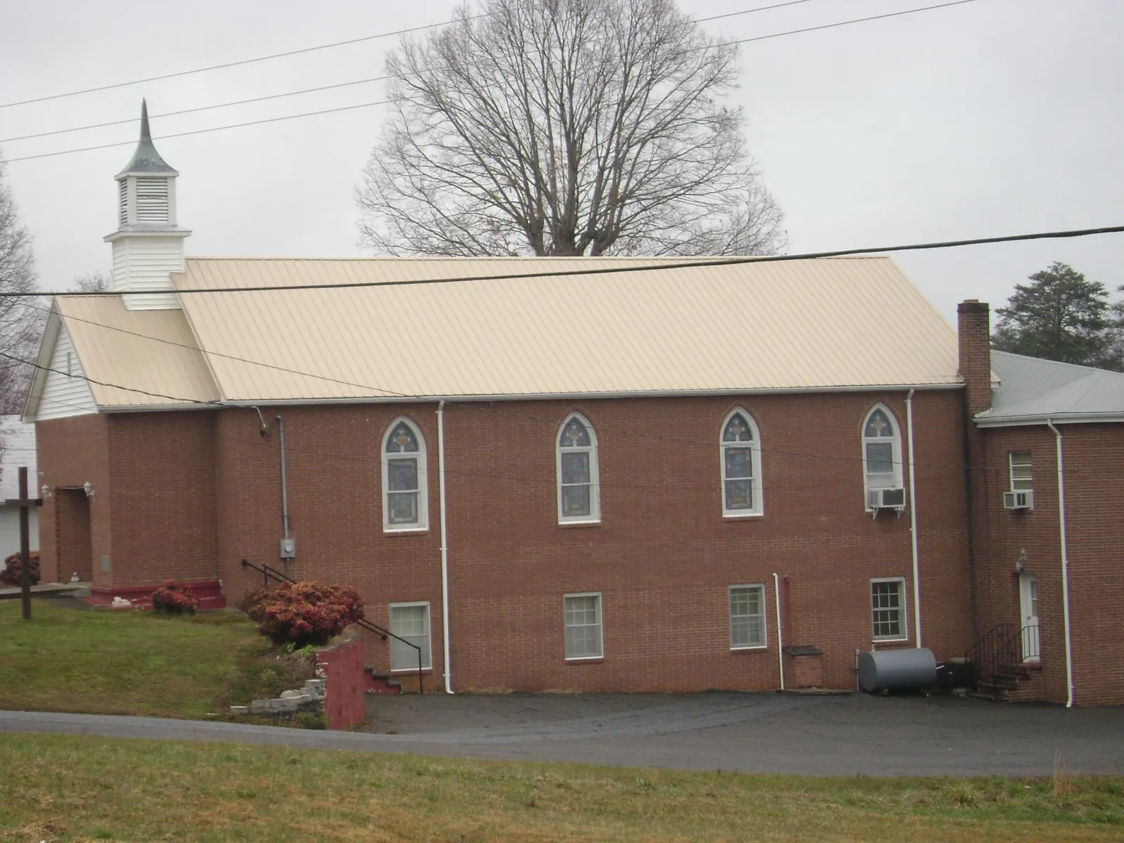 New tan metal roof on a brick church with a white steeple in Burgoon
