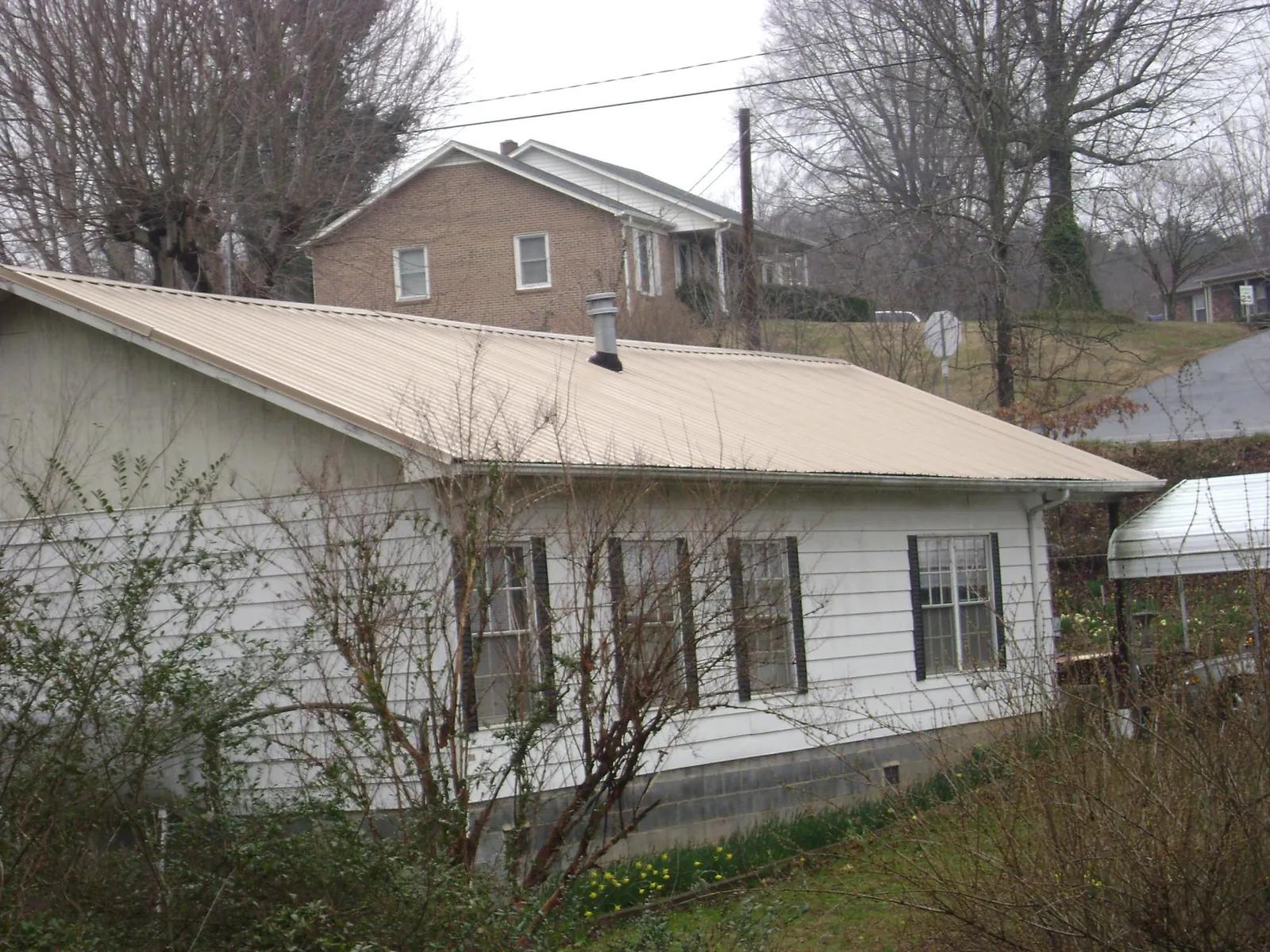 Tan metal roof on a white sided house set into a hillside — Commercial Roofing by Roofing Brothers in Burgoon
