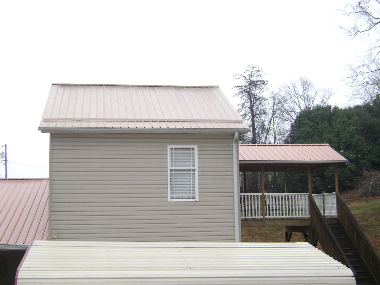 Tan metal roofs on a two story addition and attached porch, from a Roof Replacement job in Burgoon